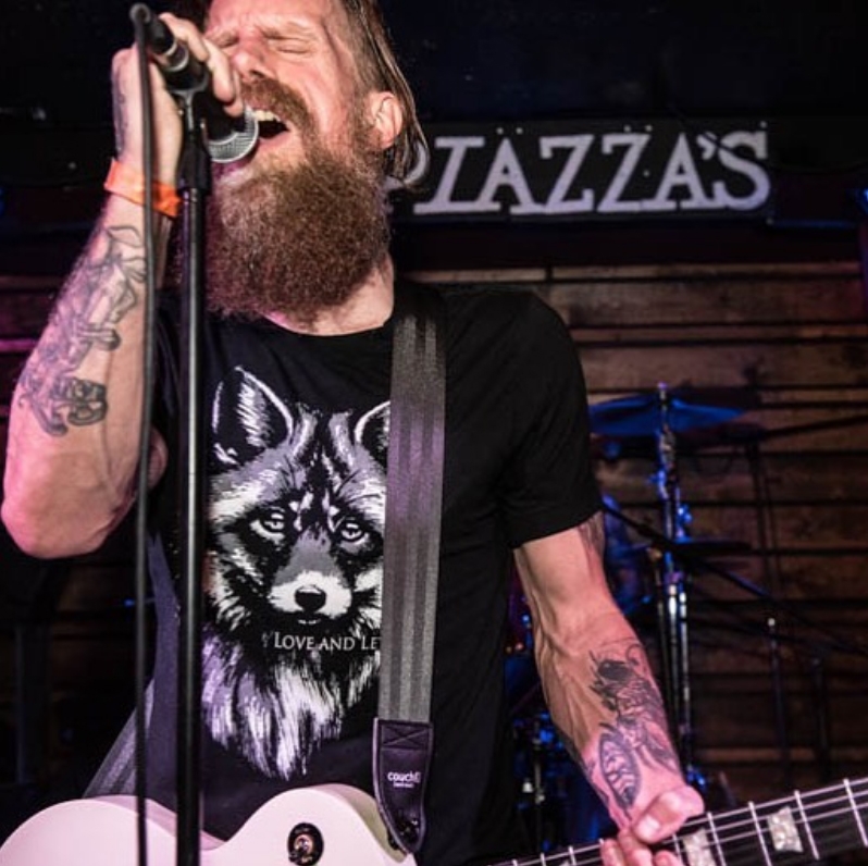 A musician performing on stage wearing the Plain Black seatbelt guitar strap