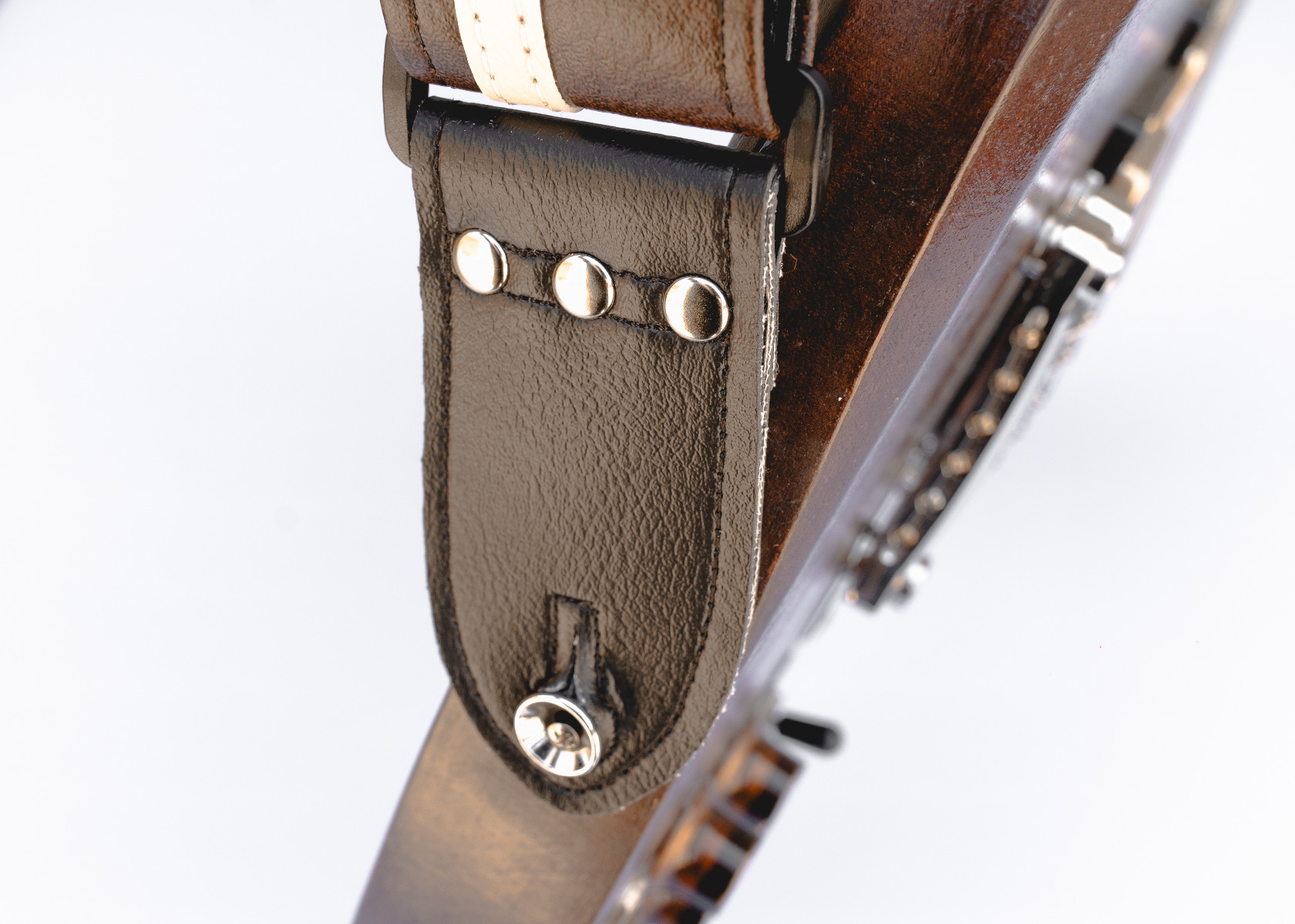 Close-up of a Couch brown and white vinyl guitar strap's black end tab, riveted onto a guitar's strap button