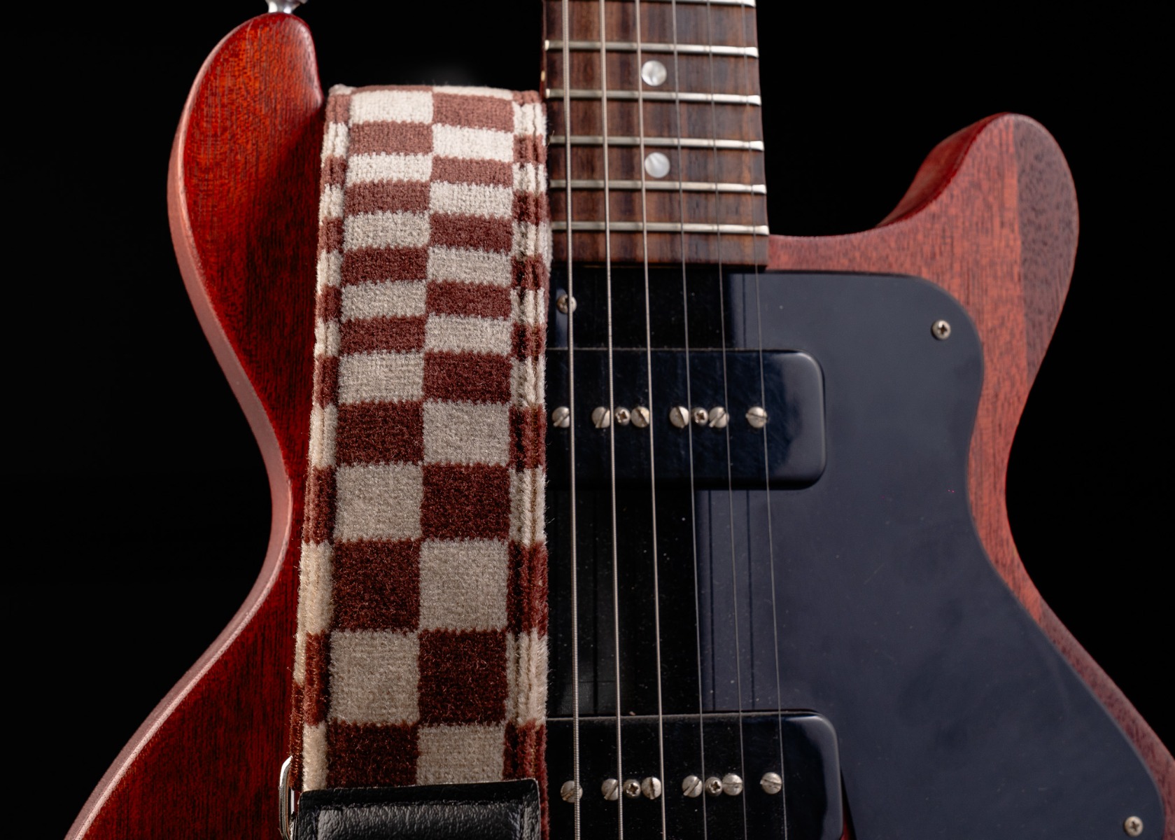 The Pasha guitar strap in burgundy and white against a cherry electric guitar