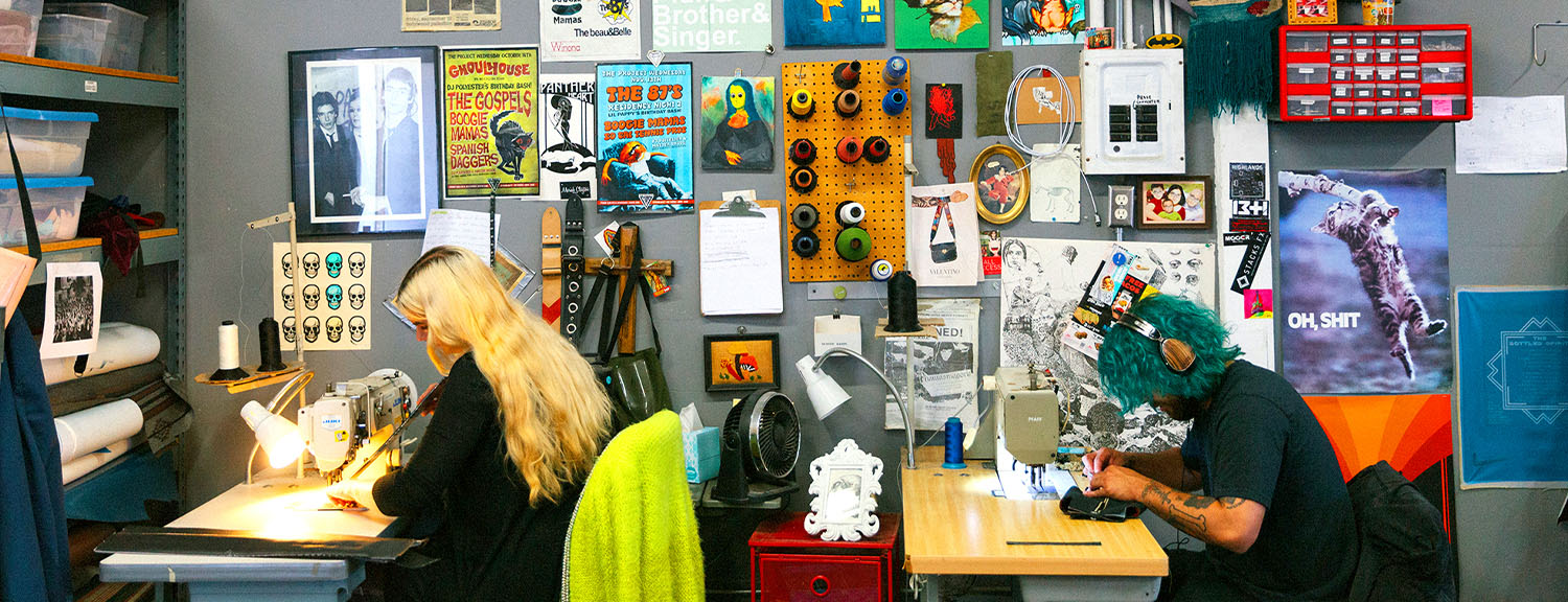 Couch founder Daniel Perkins hand-sewing a guitar strap, alongside a stack of vintage vinyl strap samples and a press clipping about Couch's vegan straps
