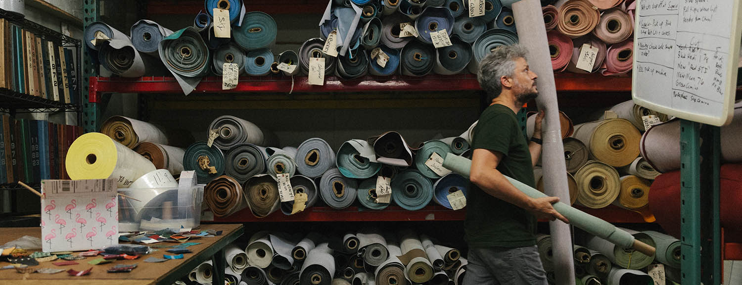 Couch team member carrying a roll of vinyl past shelves stacked with material samples