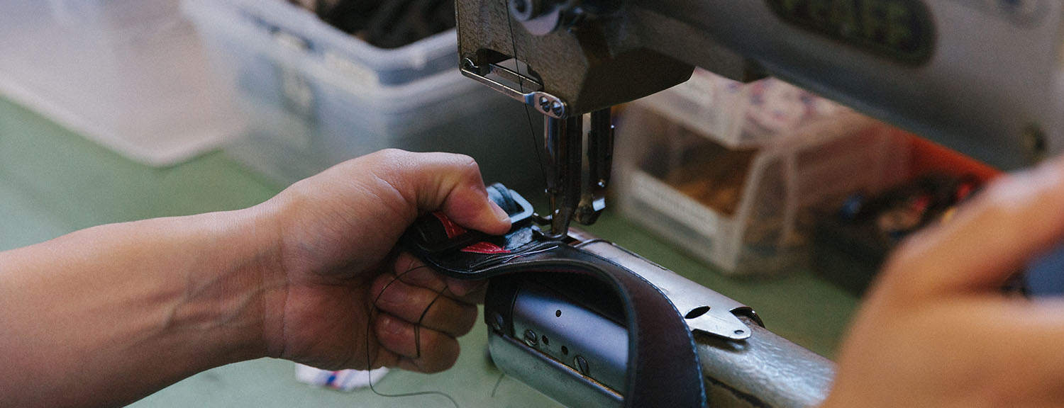 Close-up of hands guiding a guitar strap through an industrial sewing machine